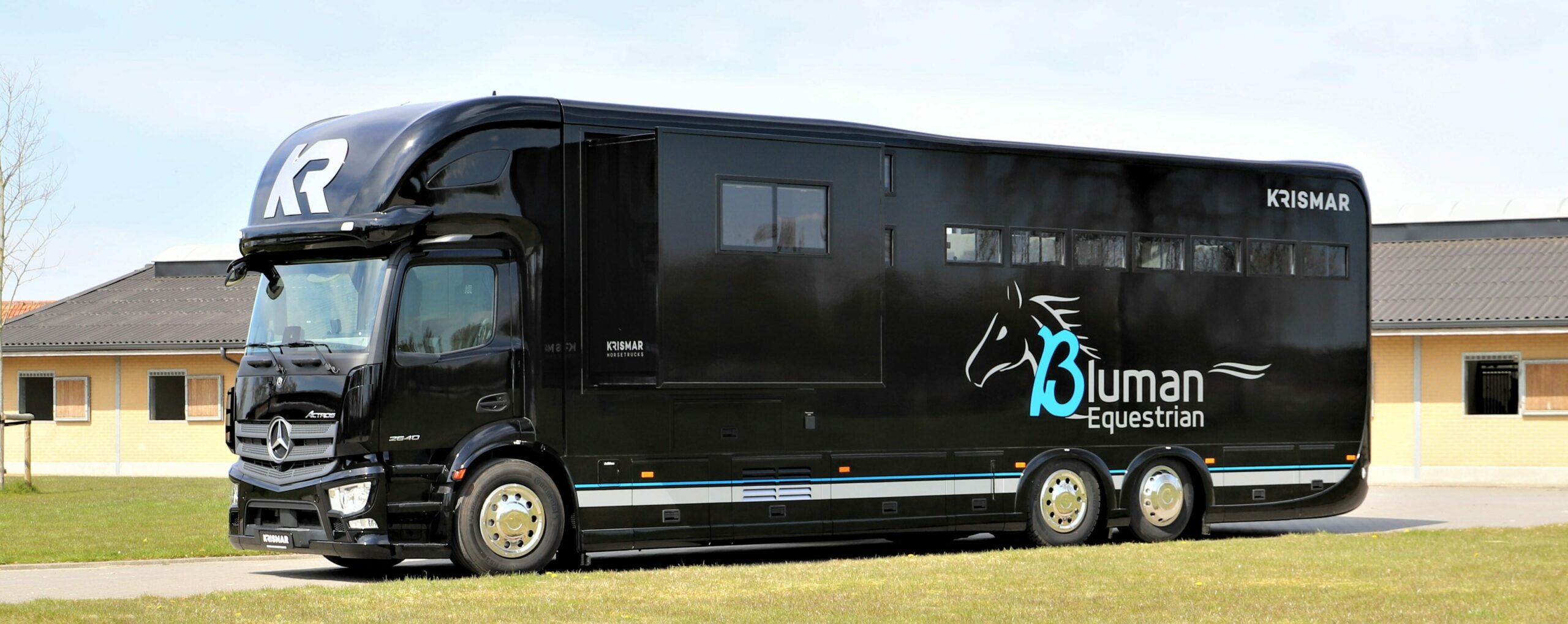 Een zwarte paardenvrachtwagen met logo van Bluman Equestrian