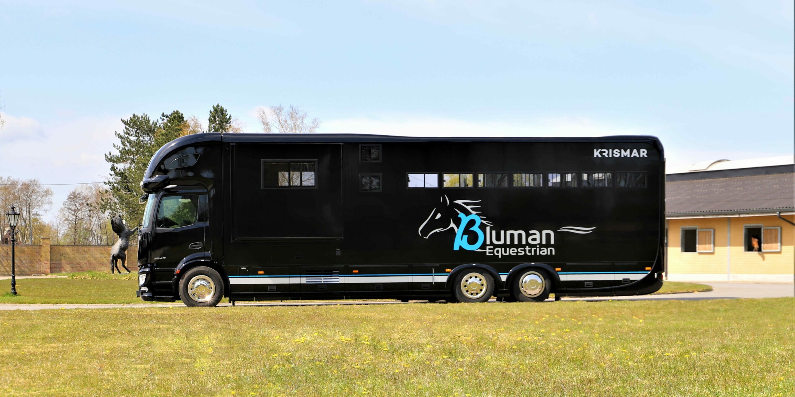 Een zwarte paardenvrachtwagen met logo van Bluman Equestrian
