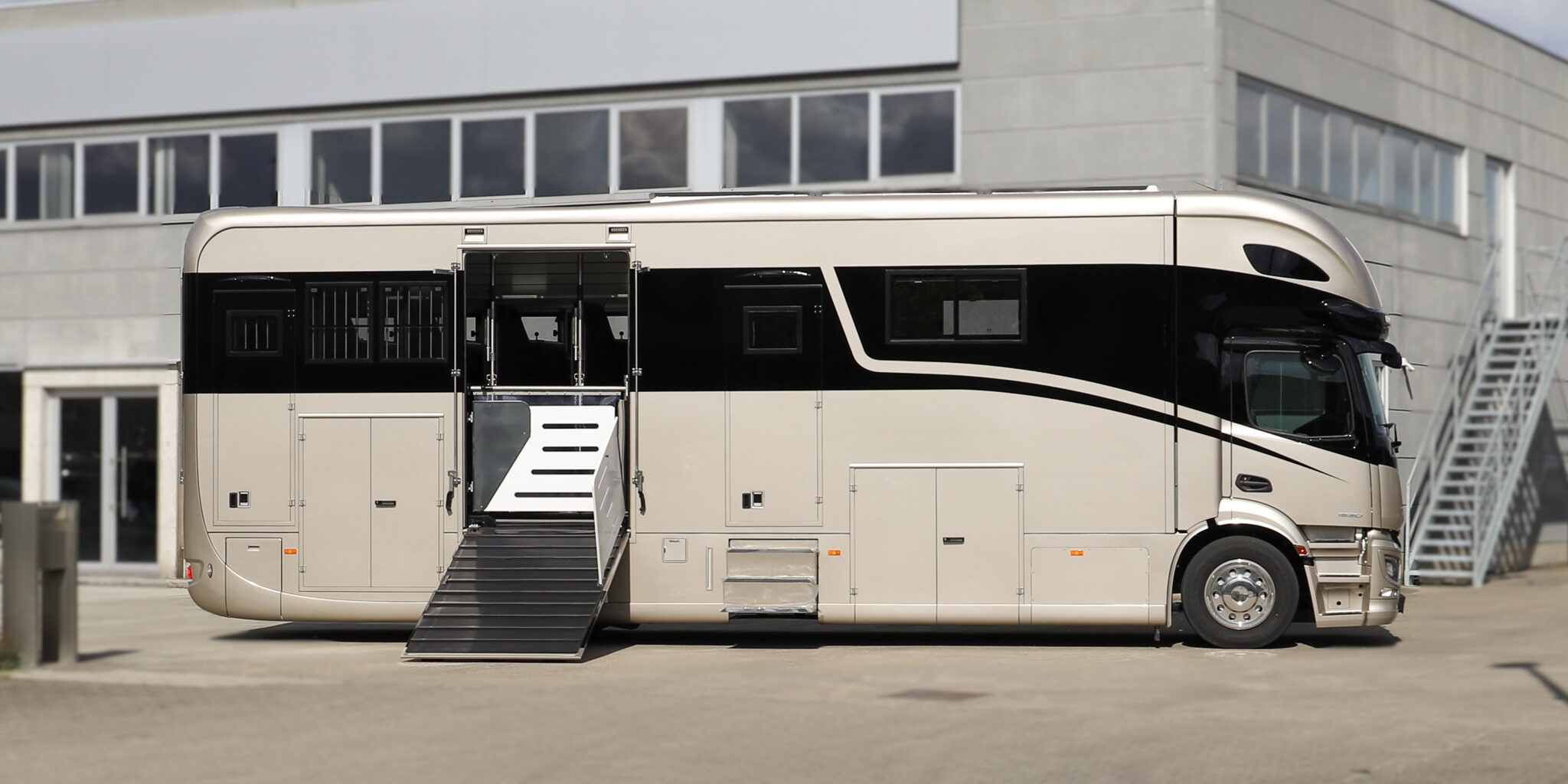 Side view of a Krismar horse truck painted in a gold color with the loading ramp on the side open.